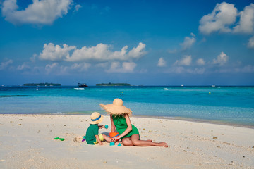 Fototapeta na wymiar Family on beach, woman in green dress with three year old boy. Summer vacation at Maldives.