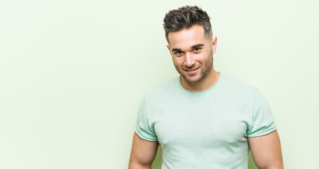 Young handsome man against a green background happy, smiling and cheerful.