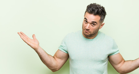 Naklejka premium Young handsome man against a green background doubting and shrugging shoulders in questioning gesture.