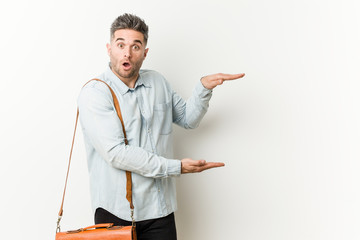 Young handsome business man shocked and amazed holding a copy space between hands.