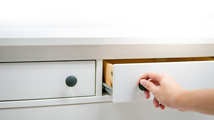 Male hand pulling and opening drawer on white wooden cabinet. Home furniture and decoration...