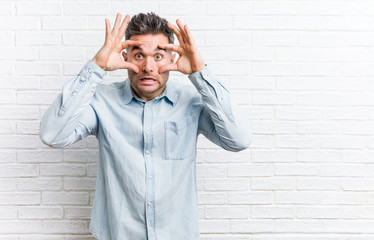 Young handsome man against a bricks wall keeping eyes opened to find a success opportunity.