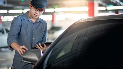 Young Asian auto mechanic holding digital tablet checking car wing mirror. Mechanical maintenance engineer working in automotive industry. Automobile servicing and repair concept