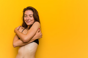 Young european woman wearing bikini hugs herself, smiling carefree and happy.