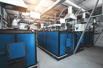 water-heating solid fuel boilers installed in a row in boiler room. Pipe and pipelines. Blue toning with sunflare