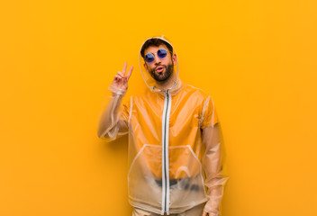 Young man wearing a rain coat fun and happy doing a gesture of victory