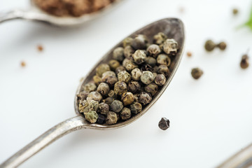 close up view of pepper in silver spoon on white background
