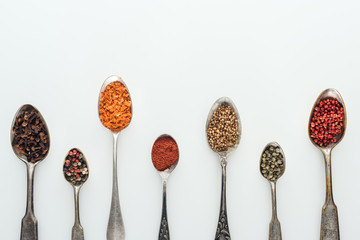 top view of colorful spices in silver spoons on white background with copy space