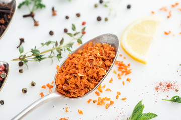 close up view of candied fruit in silver spoon near herbs and spices on white background