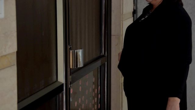 Woman comes to the outside door of a residential building.  She is assured there are a lot of microbes on the door handle, therefore, she applies a hygiene napkin on it. Then she opens the entrance do
