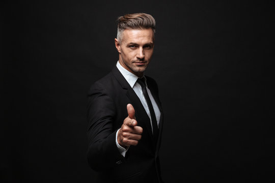 Portrait of serious manly businessman dressed in formal suit pointing finger and looking at camera