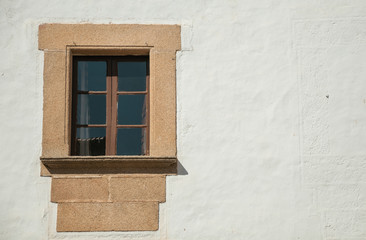 Lonely small window with stone garnish on a wall painted in white at Caceres