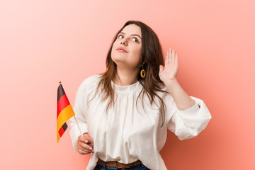 Young curvy plus size woman holding a germany flag trying to listening a gossip.