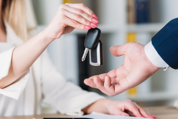 cropped shot of woman taking car keys from car dealer in office