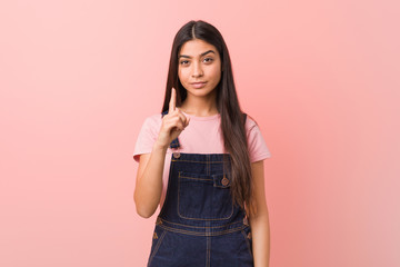 Young pretty arab woman wearing a jeans dungaree showing number one with finger.