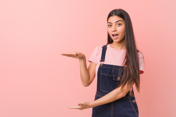 Young pretty arab woman wearing a jeans dungaree shocked and amazed holding a copy space between hands.