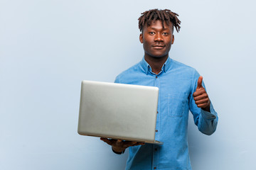 Young rasta black man holding a laptop smiling and raising thumb up