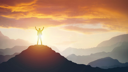 Man standing on edge of mountain feeling victorious with arms up in the air.