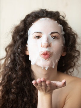 Beautiful young woman is applying a cosmetic tissue mask on a face on a white background 