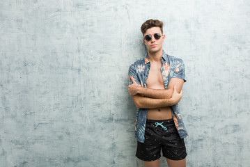 Young caucasian man wearing a swimsuit who feels confident, crossing arms with determination.