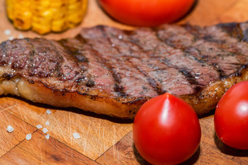 Close up freshly grilled steak on wood with tomatoes and corn