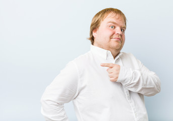 Young authentic redhead fat man smiling and pointing aside, showing something at blank space.