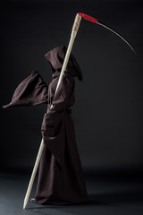 side view of woman in death costume holding scythe on black