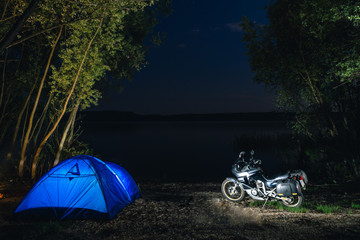 Blue Camping Tent Illuminated Inside. Night Hours Campsite. Recreation. Motorcycle traveler, tourist bikers. lake and stars. take a rest after long riding. Equipment for travel. Campfire, bonfire