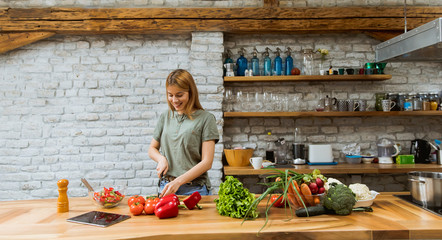 Happy young woman cooking delicious and healthy food in the loft kitchen at home