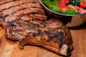 Close up freshly grilled bone steak on wood and fresh salad in bowl