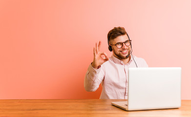 Young man working in a call center cheerful and confident showing ok gesture.