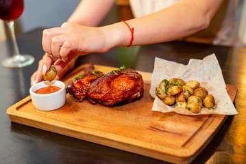 Close up woman eats smoked chicken thights served with potato in restaurant