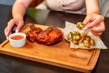 Close up woman eats smoked chicken thights served with potato in restaurant