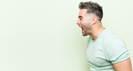 Young handsome man against a green background shouting towards a copy space