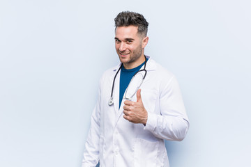 Young handsome doctor man smiling and raising thumb up