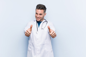 Young handsome doctor man with thumbs ups, cheers about something, support and respect concept.