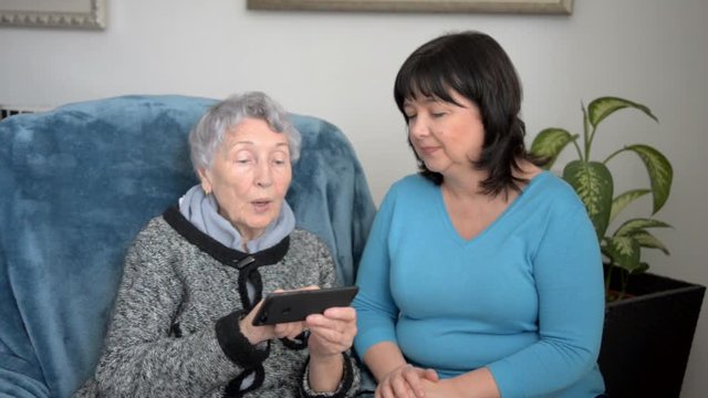 Mature female volunteer teaching an older woman how to use a smartphone. The senior woman can socialize with her friends and family which will indeed make her feel good.