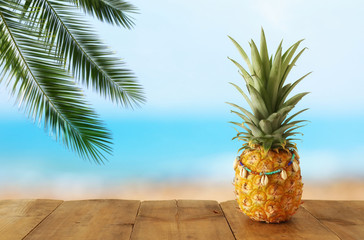 Ripe pineapple over wooden table in front of beach and tropical background