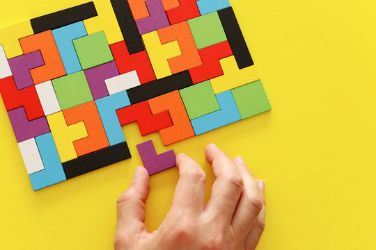 Man's Hand Holding A Square Tangram Puzzle, Over Wooden Table