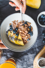 Girl holds a breakfast bowl with crunchy granola, fresh blueberry, mango and chia seeds. Flat lay, top view, healthy eating.