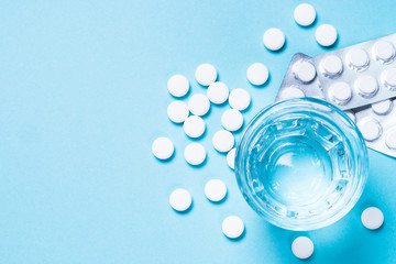Pills and glass of water on blue top view.