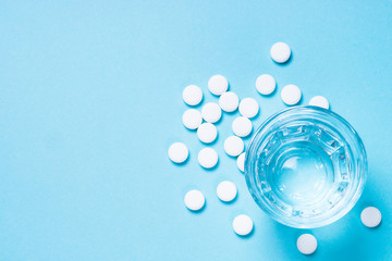 Pills and glass of water on blue top view.