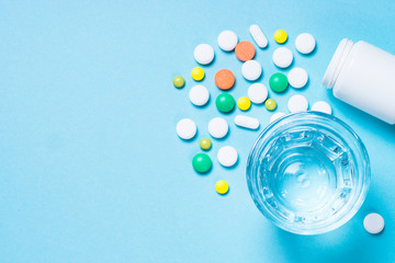 Pills and glass of water on blue top view.