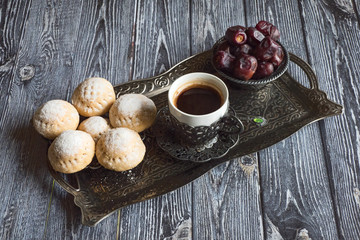 Top view on silver plate with sweets, date fruits and coffee cup on the dark wooden table. Ramadan background
