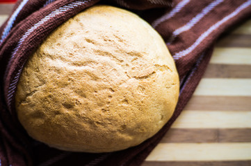 White, freshly baked bread in a towel on a wooden board