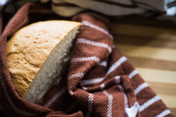Freshly baked bread cut in half wrapped in a towel on a bamboo board