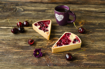 Mini tarts with cherries and cream with cup of black tea on dark wooden background