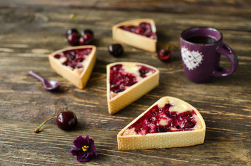 Set of mini tarts with cherries and cream with cup of black tea on dark wooden background