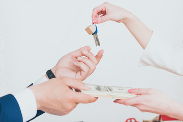 cropped view of client holding keys while giving dollar banknotes to realtor