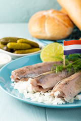 Traditional dutch food freshly salted herring fish with onion called hollandse nieuwe on turquoise plate and wooden background. European food concept.
